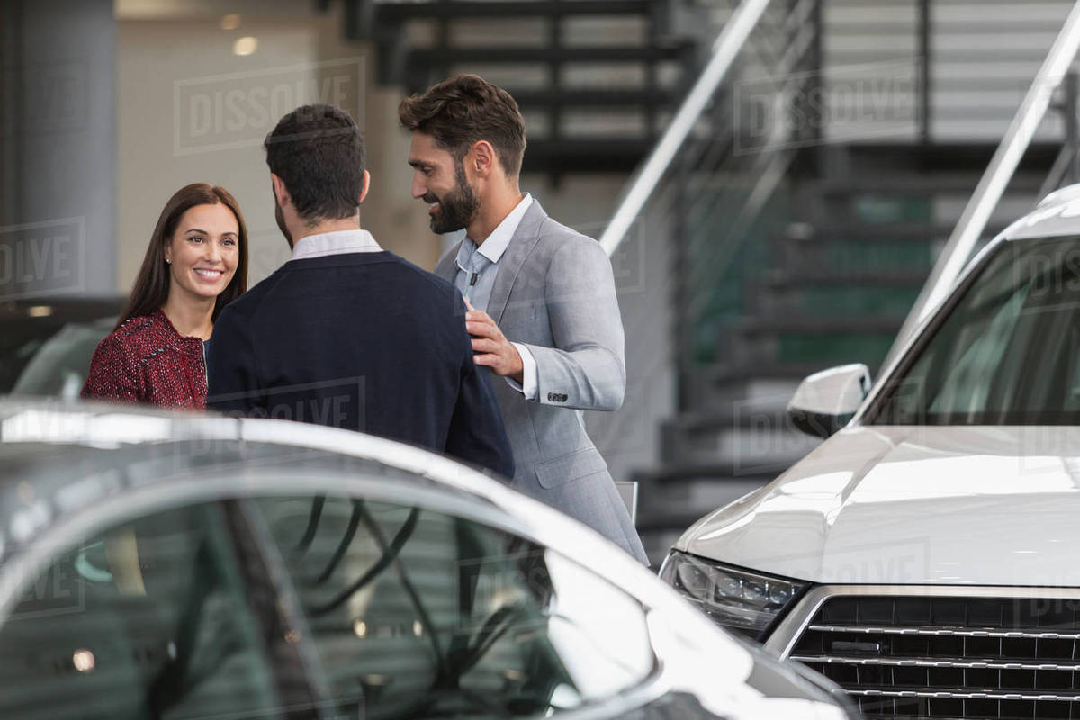 Car salesmen talking to female customer in car dealership showroom