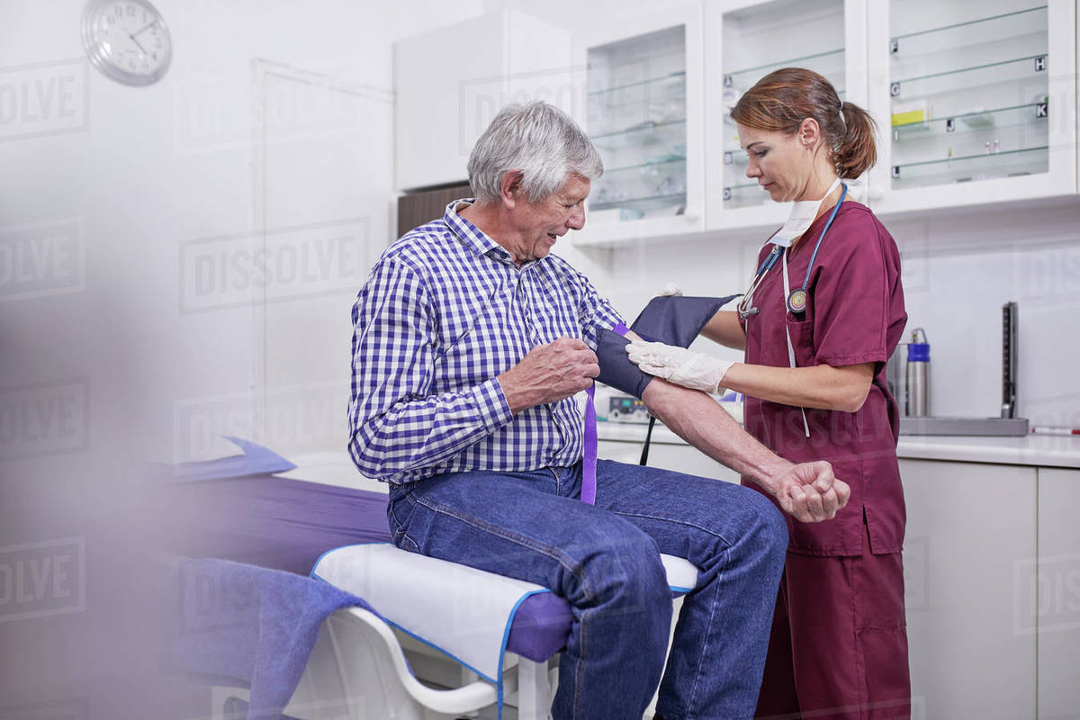 Female nurse checking blood pressure of senior male patient in clinic