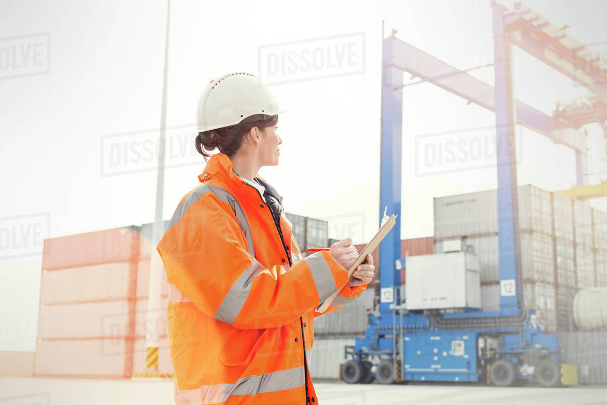 Female dock manager with clipboard watching cargo containers Stock