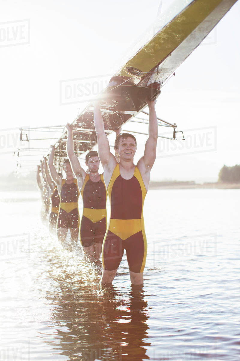 Rowing team carrying scull overhead in lake Stock Photo Dissolve