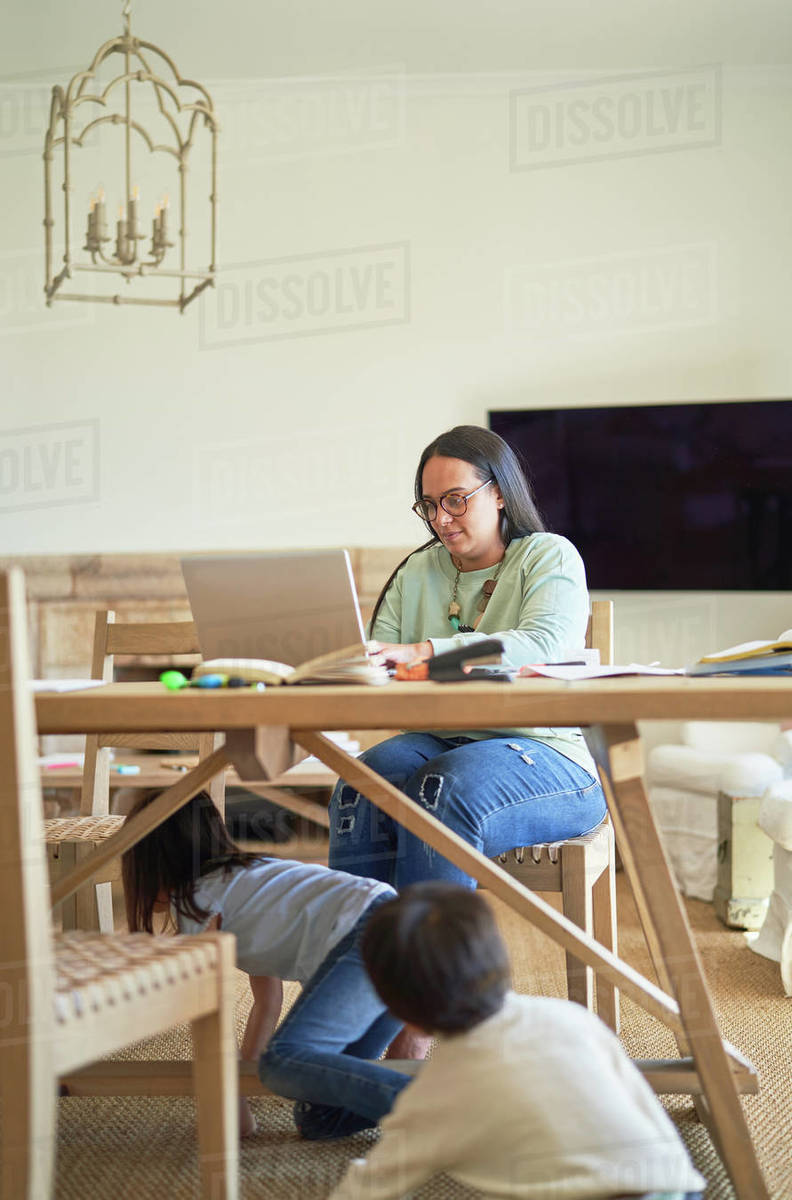 Kids playing under table while mother works at laptop - Royalty-free ...