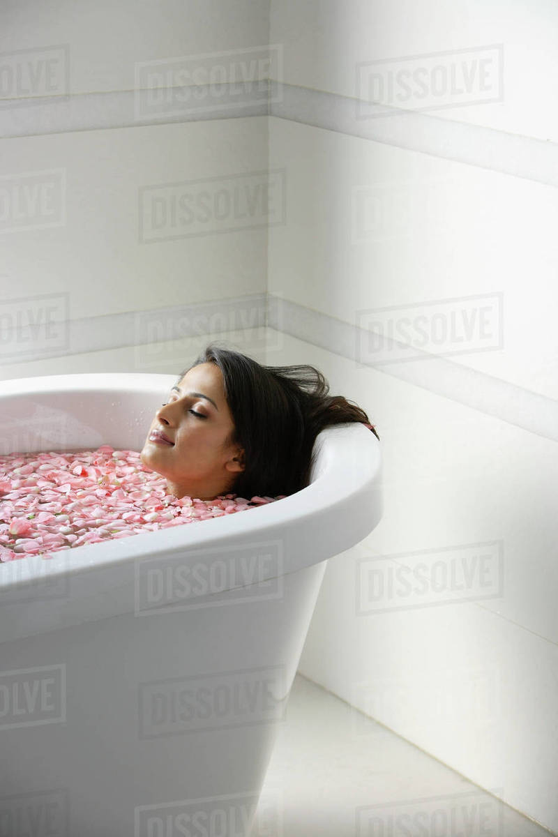 Woman in bath tub with floating petals Stock Photo Dissolve