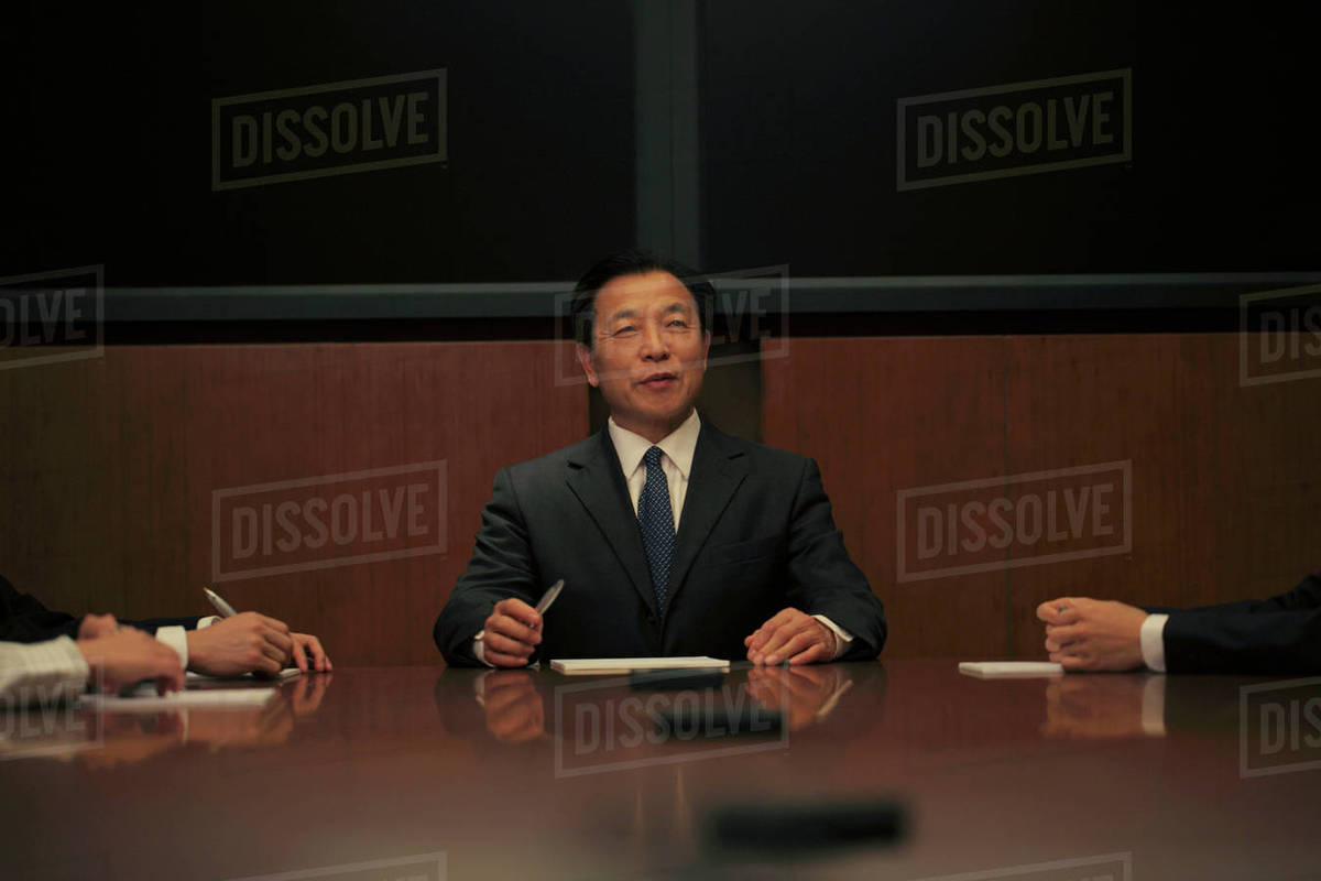 Businessman sitting at head of the table Stock Photo Dissolve