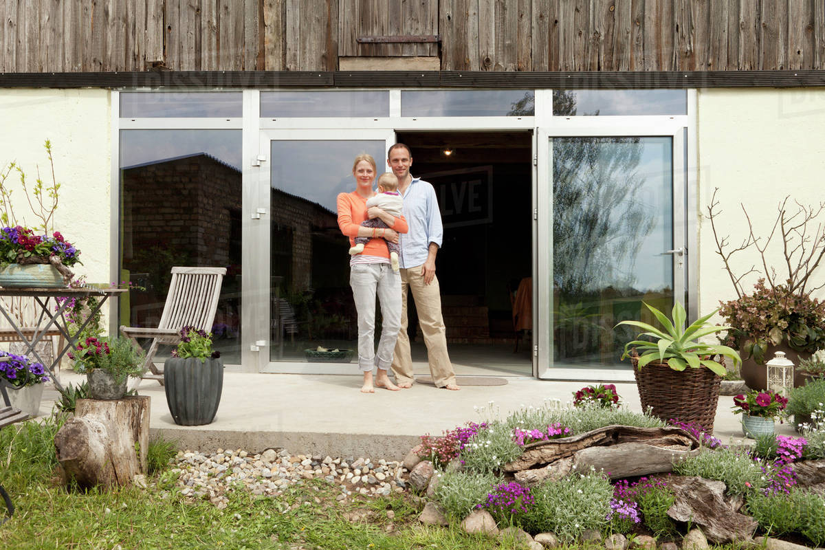 A man and a woman holding a baby standing on the patio in front of their house Royalty-free stock photo