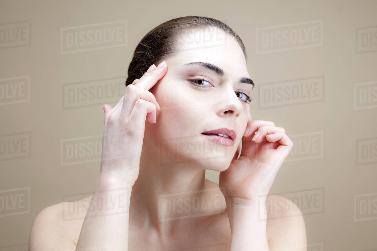A young woman with her fingers on her temples pulling the skin back Stock Photo Dissolve