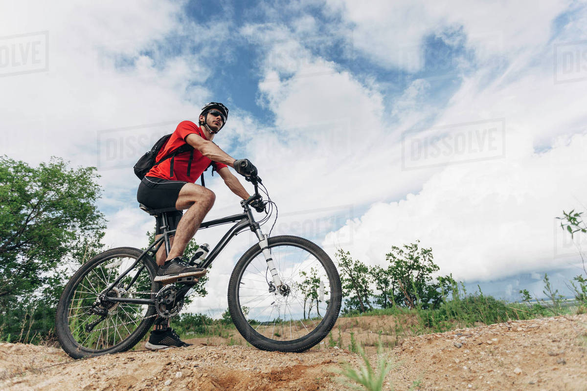 Low angle view of man riding mountain bike in rural setting against sky