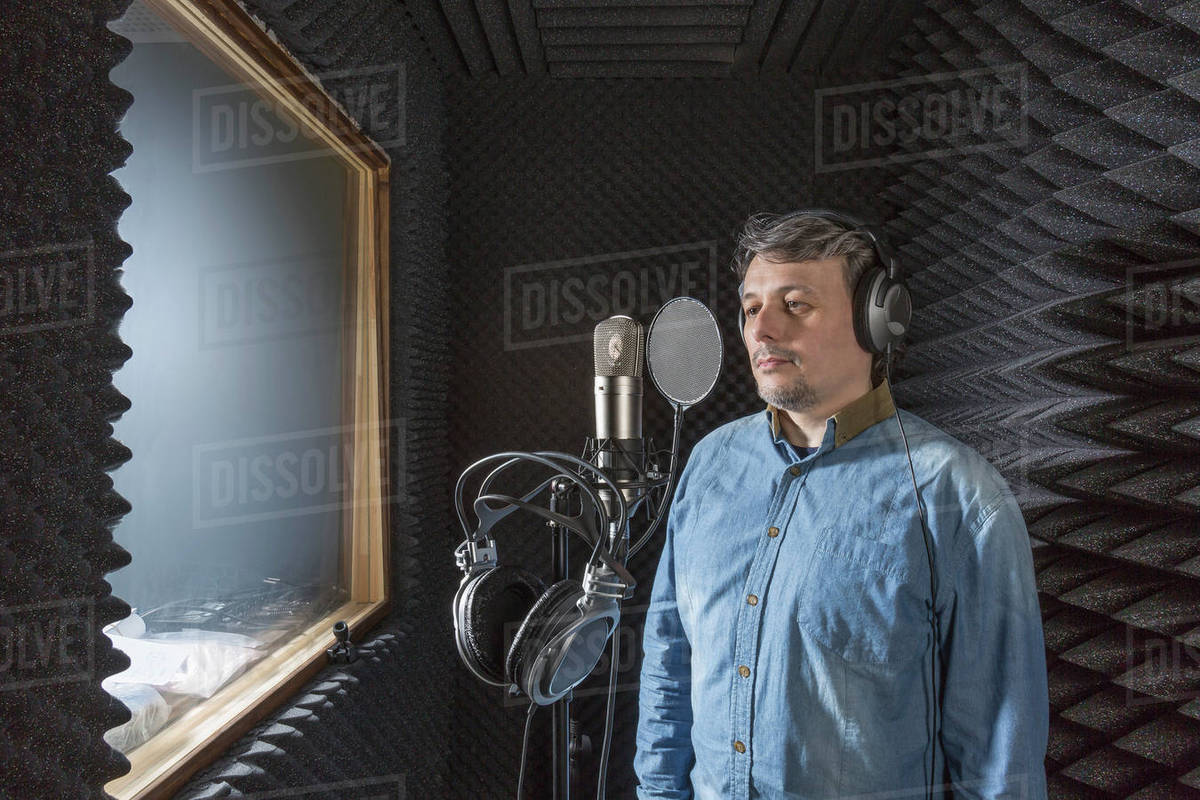 Musician standing by microphone with headphones in recording studio