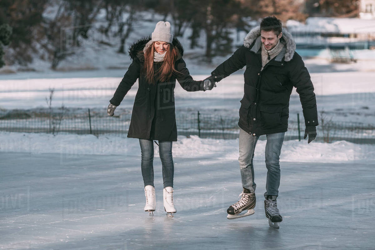Full length of man holding hands with woman while enjoying iceskating