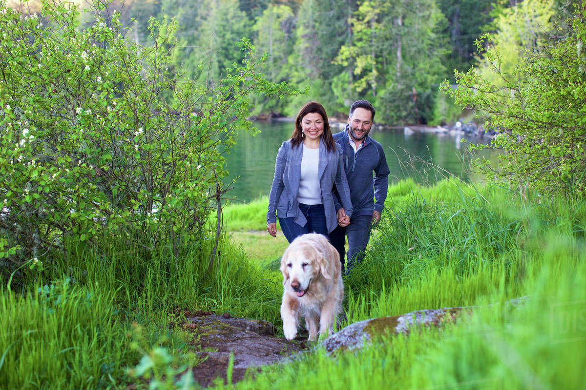 Happy couple with dog hiking along lush green lakeside, Mill Bay, British Columbia, Canada Royalty-free stock photo