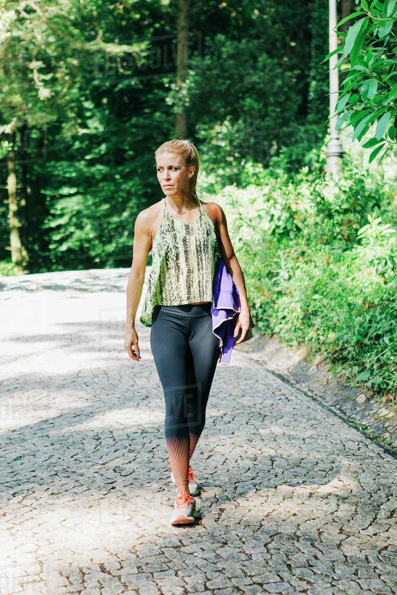 Fit female personal trainer walking on cobblestone path in park Royalty-free stock photo