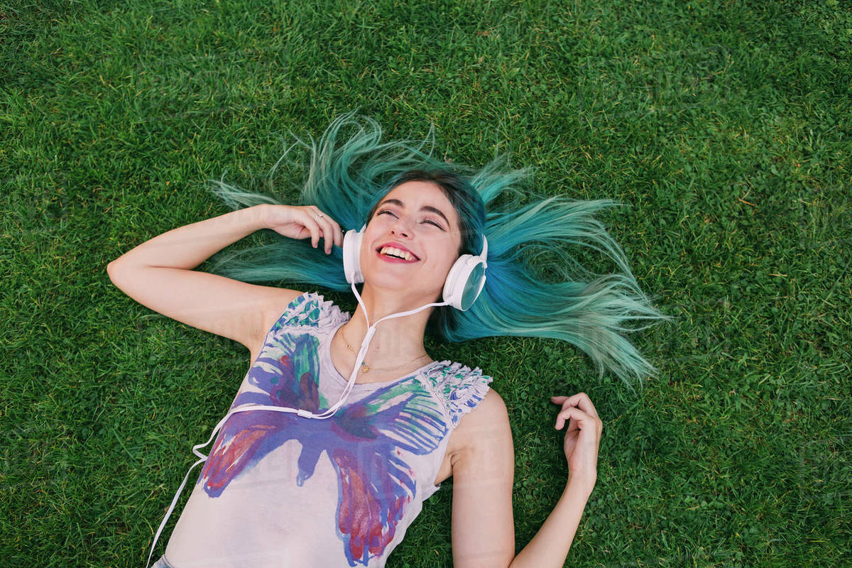 Happy, carefree young woman with blue hair listening to music with headphones, laying in grass Royalty-free stock photo