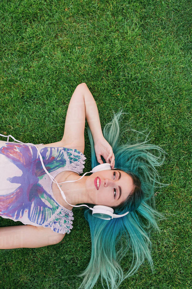 Overhead portrait young woman with blue hair listening to music with headphones, laying in grass Royalty-free stock photo