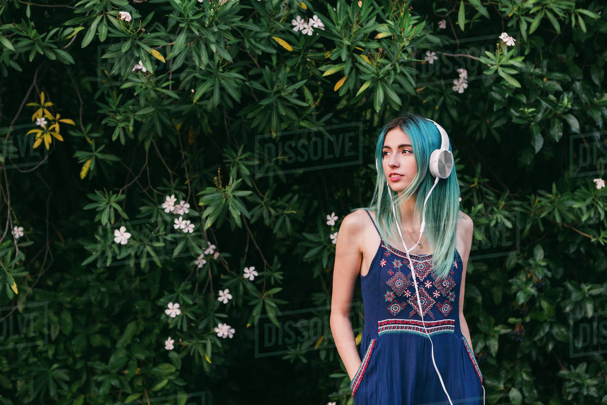 Young woman with blue hair listening to music with headphones in front of flowering tree Royalty-free stock photo