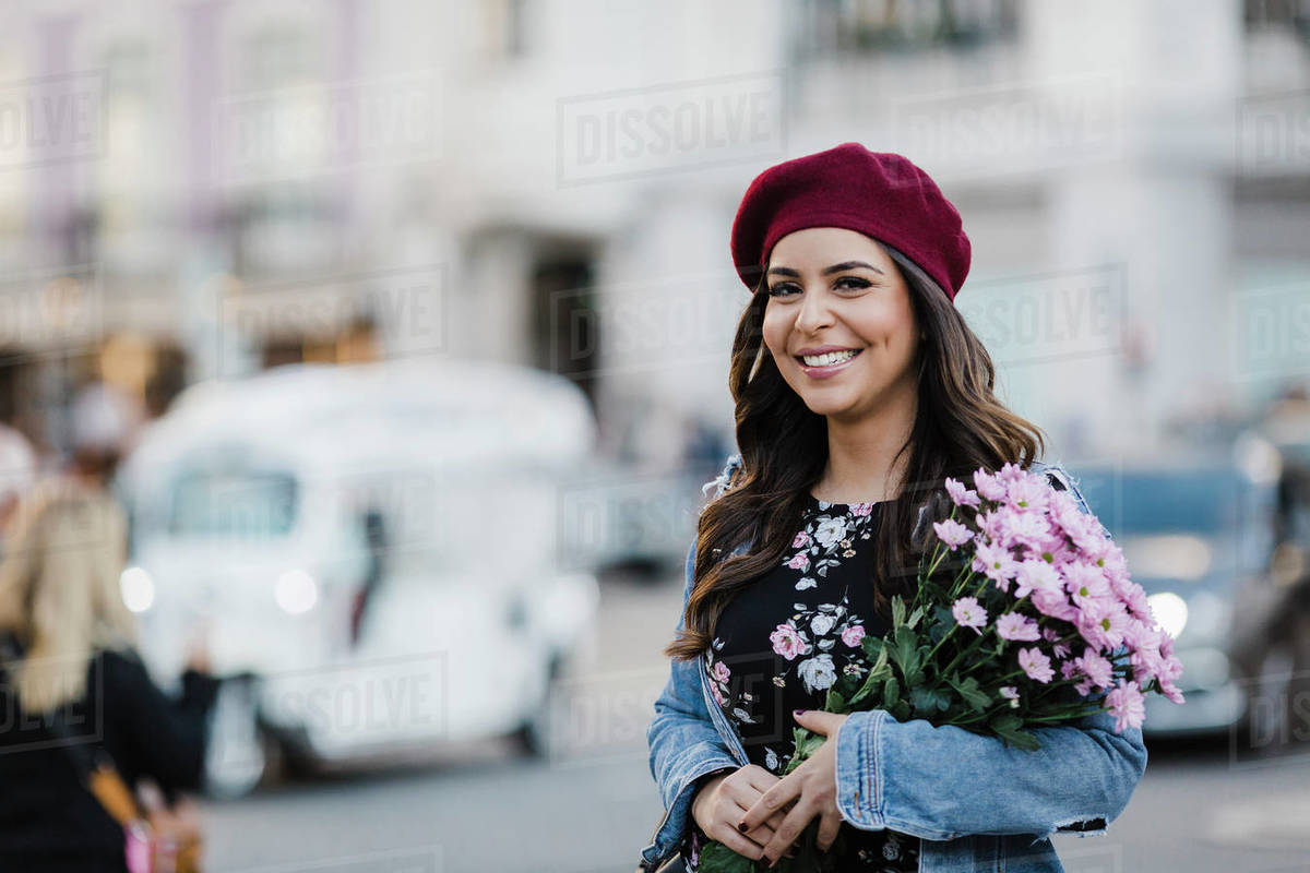 Portrait happy young woman in beret with flower bouquet on urban street Royalty-free stock photo