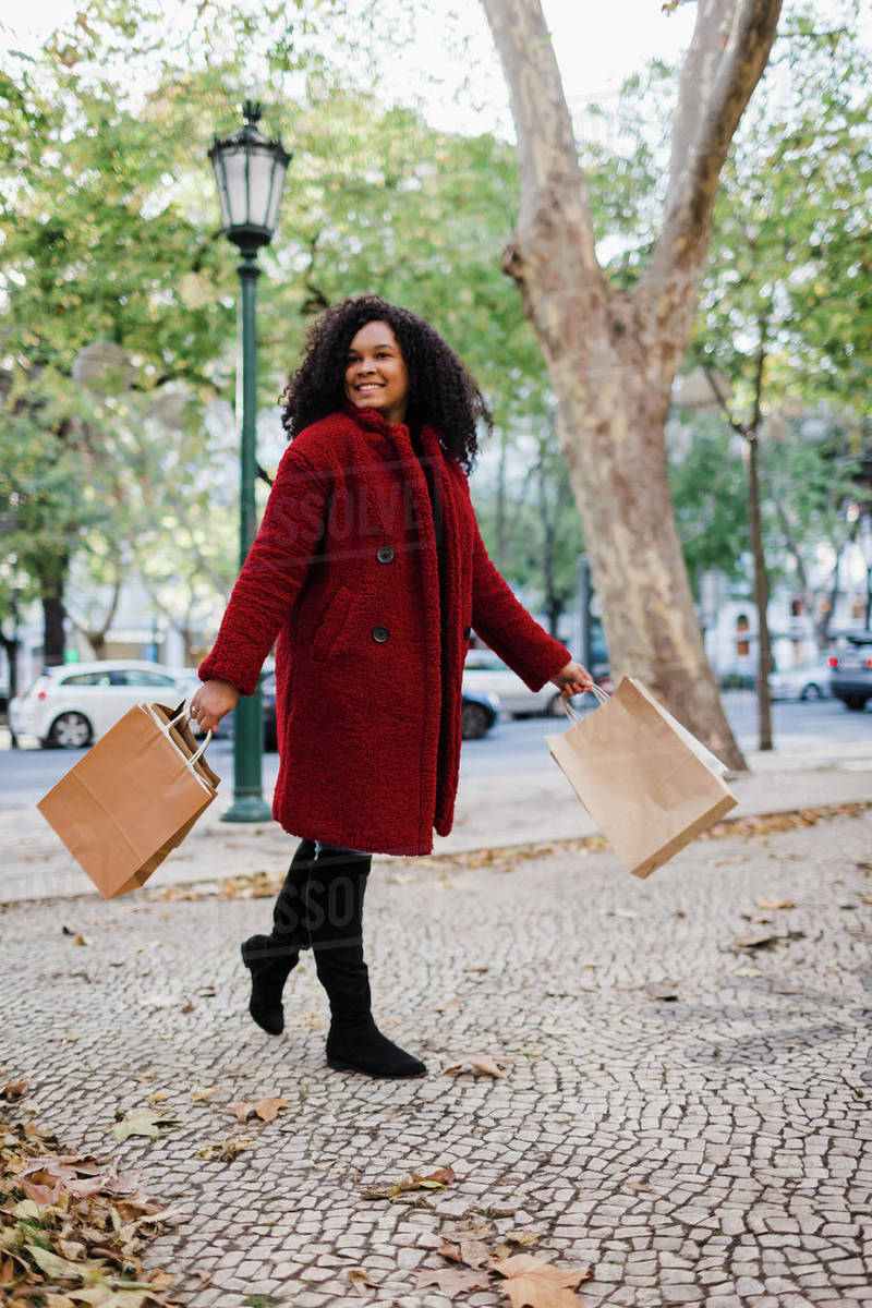 Portrait carefree young woman walking with shopping bags in urban autumn park Royalty-free stock photo