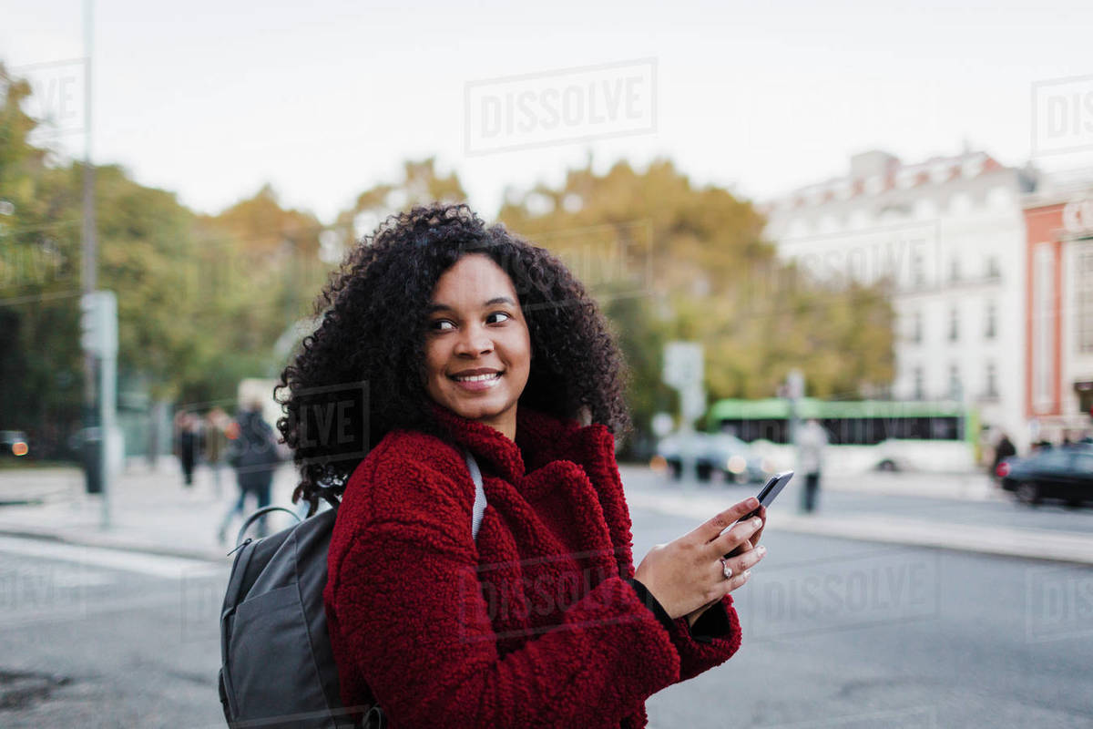 Smiling young woman with smart phone looking over shoulder on city street Royalty-free stock photo